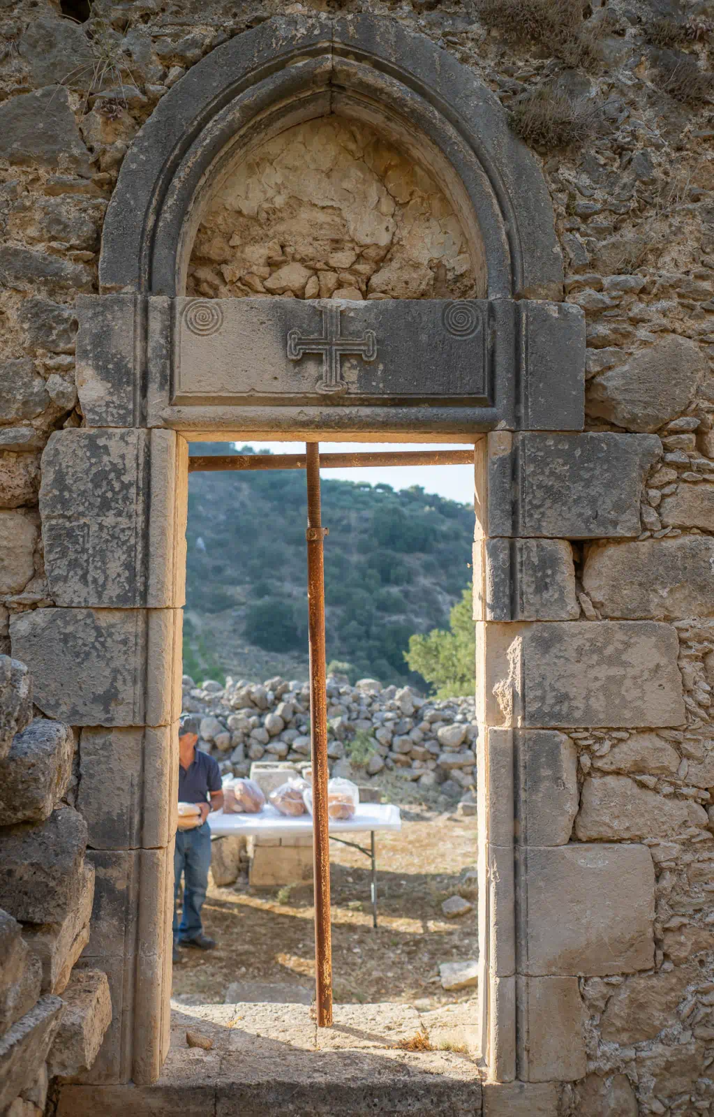 Side entrance of the church of Agios Antonios in Petali. The lintel is decorated with a carved cross. Above the lintel are two arches made of dressed stone. The side entrance is made up of two arches, a lintel, five dressed stones on the left, and six dressed stones on the right. There are small square holes in the interior side of the entrance, which were likely used for the formwork in the construction phase.